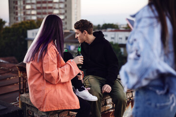 A teenage friends on a rooftop party drinking beer and chatting.