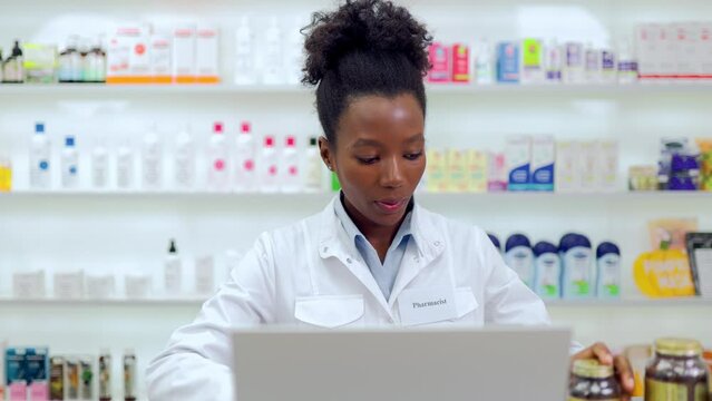 African american female pharmacist in white lab coat working on modern computer at bright drugstore full of various medication. Technology and pharmaceutics concept.