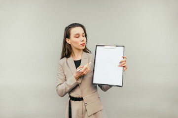 Naklejka premium Business woman with a tablet in her hands stands on a beige background looks at a blank white sheet of paper and shows a pen on copy space