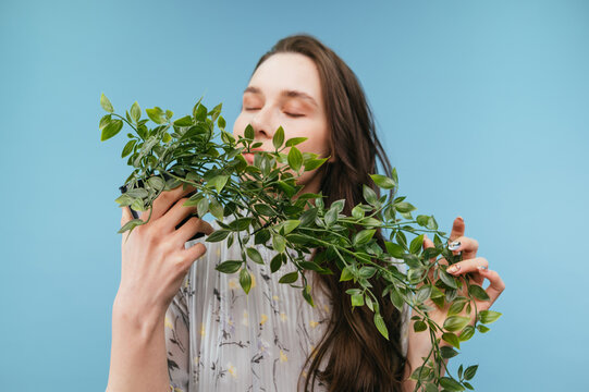 Cute lady in a dress holding a curly plant sniffing it with closed eyes on a blue background.