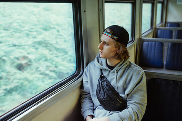 Handsome young man in casual clothes rides in a train and looks out the window.