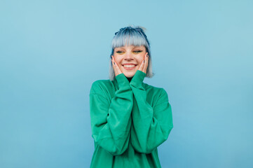 Joyful girl with blue hair stands on a green background with a smile on his face and happy looks away. - Powered by Adobe