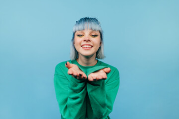 Portrait of a joyful hipster girl with blue hair stands on a blue background with a smile on his...