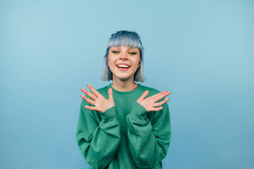 Joyful girl with colored hair stands on a blue background with a happy face looking at the camera
