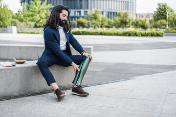 Business man adjusting his prosthetic leg outdoor from office building - Job and insurance concept - Focus on hands holding prosthesis