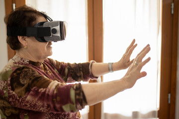 Caucasian aged mature woman exploring or playing in virtual augmented reality with vr goggles headset in the Metaverse. Futuristic world concept