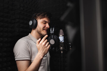 man sings into microphone, professional recording studio, headphones. Black soft walls, sound...