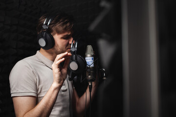 man sings into microphone, professional recording studio, headphones. Black soft walls, sound...