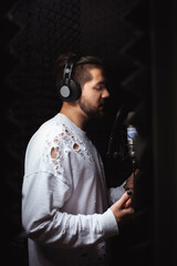 man sings into microphone, professional recording studio, headphones. Black soft walls, sound insulation. singer records his song. white jacket
