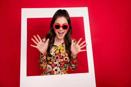 Photo of shiny impressed young lady dressed flower print outfit glasses standing inside photo frame isolated red color background