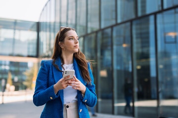 Modern businesswoman in blue suit using mobile phone. Looking away. Copyspace