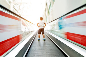 Rear view of litlle boy on moving escalator