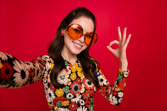 Photo of cute sweet young lady dressed flower print outfit glasses recording video showing okey sign isolated red color background