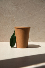 Zero waste concept. Paper glass on a stone beige background with a green leaf. Front view