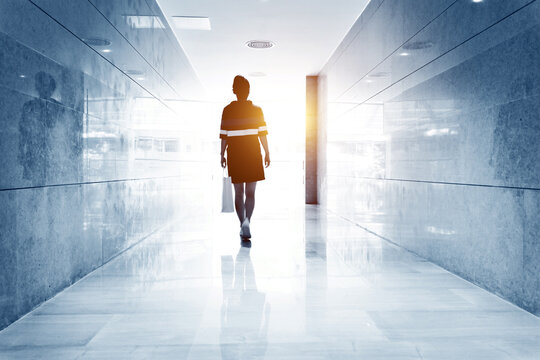 Woman Walking Down A Corridor Towards Lit Exit