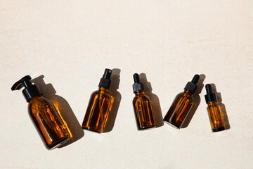Clear brown bottles with natural cosmetics on a beige stone background. Flat lay