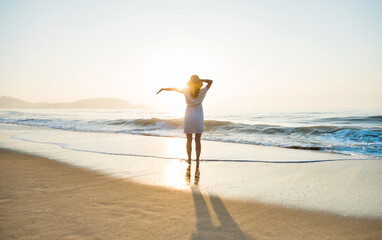 Happy woman standing on the beach with arms outstretched.