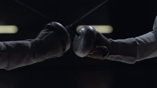 CU Two professional male fencers having a sabre fight in against dark background