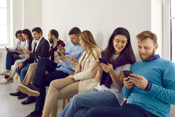 Happy young people using cellphones. Group of different millennial people sitting in row, holding modern mobile phones, using social media apps, scrolling feed, watching funny videos, looking at memes - obrazy, fototapety, plakaty
