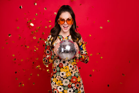 Portrait of attractive cheerful girly girl holding silver disco ball having fun isolated over bright red color background