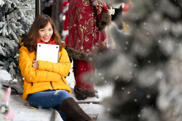 Young Asian woman hugging laptop in hands with happy and smile face while sitting on snow floor in Winter after class. Wearing yellow sweater and orange scarf to protect from cold weather.