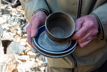 An elderly woman holds in her hands tea utensils that survived the destruction of her house as a result of the shelling of Russian troops in Irpin, Ukraine