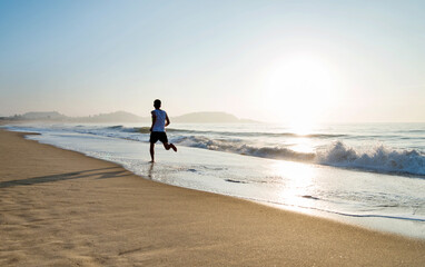 Naklejka premium Young man running along beach in the morning