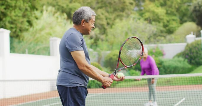 Video of happy biracial senior man holding racket and starting match on tennis court