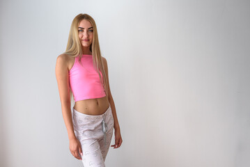 A girl in home clothes stands against a gray wall. Girl in a pink top.