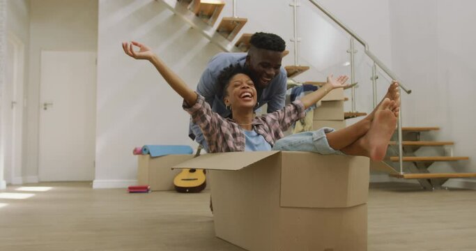 Video of happy african american couple having fun with boxes after moving into new house