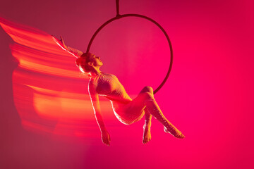Young artistic girl, professional air gymnast training, performing isolated over pink background...