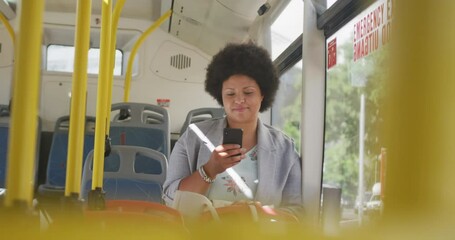 Happy plus size biracial woman using smartphone in bus - Powered by Adobe