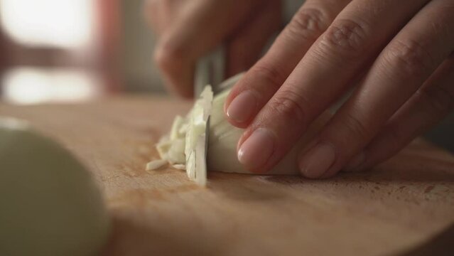 A woman cuts an onion on a wooden board.