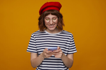 indoor portrait of young ginger female, wears stripped t shirt and glasses posing over orange background