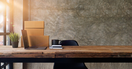 
Laptop computer at workplace of start up, small business owner. cardboard parcel box of product for deliver to customer. Online selling, e-commerce, packing concept, Morning light