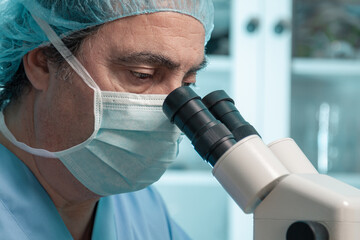 senior scientist looking through the microscope with protective mask
