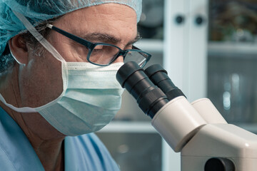 senior scientist wearing glasses looking through the microscope