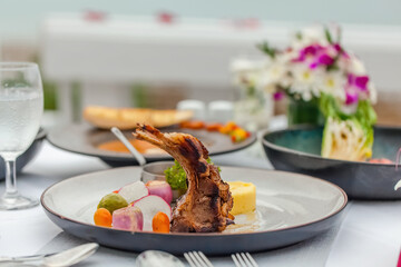 Roasted rack of lamb and vegetables garnish on white plate on table in luxury restaurant. Hot grilled lamb ribs chops with mashed potato and onions on dinner or lunch. Delicious food concept.