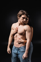Young woman touching torso of sensual boyfriend on black background.