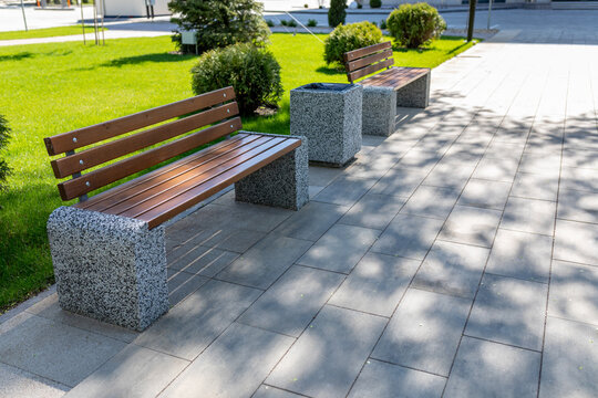 An alley with new wooden benches and garbage cans in the city square. Landscape architecture of the park