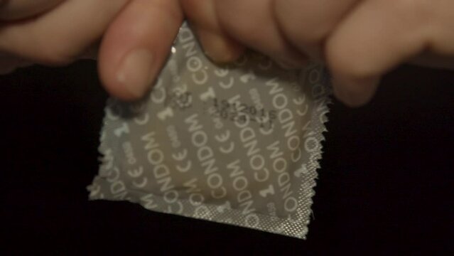 Hands struggling to open condom package