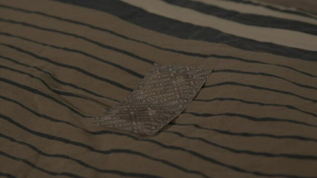 Close dolly of pair of wrapped condoms lying on pillow on bed