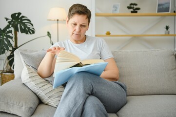 woman in home sitting on sofa reading book.