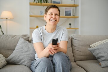 Obraz premium Portrait of happy older woman changing channel on television.
