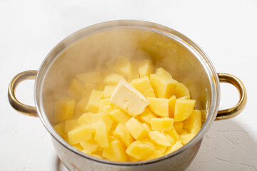 Boiled potatoes in a pot. Hot potato cubes with a piece of butter. Cooking boiled potatoes, mashed potatoes. Steam is coming. White background.