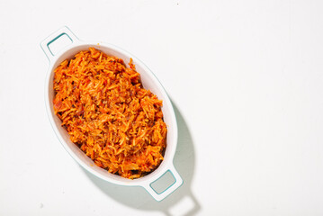 Jollof rice in a dish on a white background. Traditional Nigerian food made from rice, tomatoes and spices. Top view, place for text.