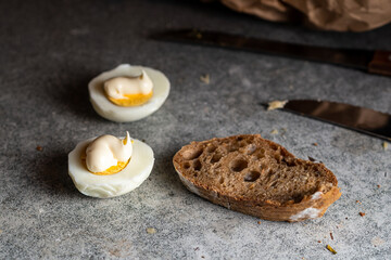 Halves of chicken eggs with mayonnaise and brown bread on a dark kitchen table.