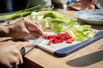 A woman cutting chili pepper and vegetables, preparing Asian cuisine. A woman cooking a homemade healthy food.