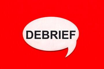 On a bright red background, a light wooden curly card with the text DEBRIEF