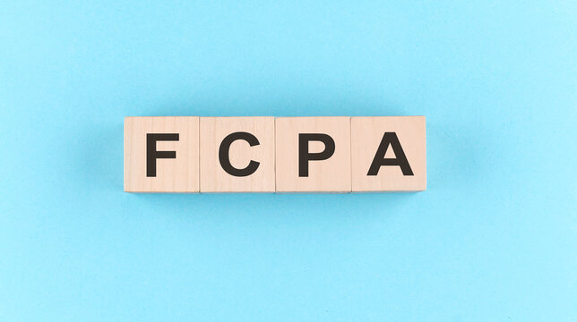 Wooden cube block with text FCPA on the blue background